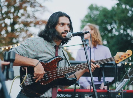 Picture of a musician performing live. His electric bass is positioned behind him with 2 keyboards on a stand in front of him. Playing multiple instruments can be a big advantage in getting gigs.